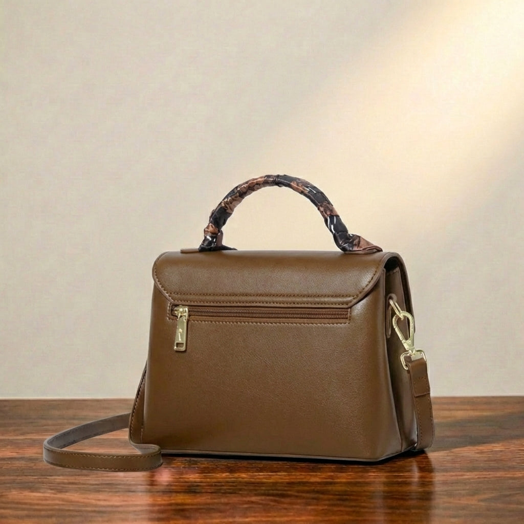 Brown leather crossbody bag shown from the back, featuring a zip pocket, placed on a wooden surface against a neutral background.