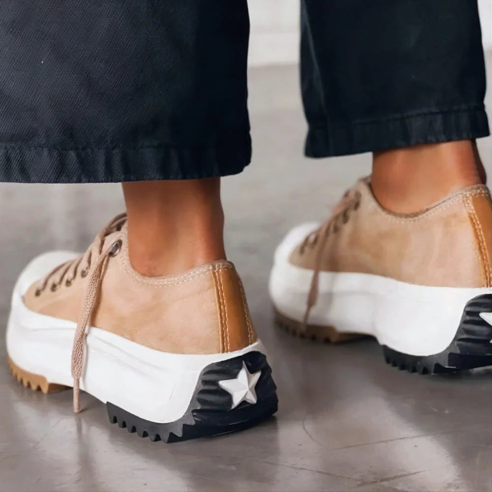 Tan and white sneakers with a star detail on a wooden floor.