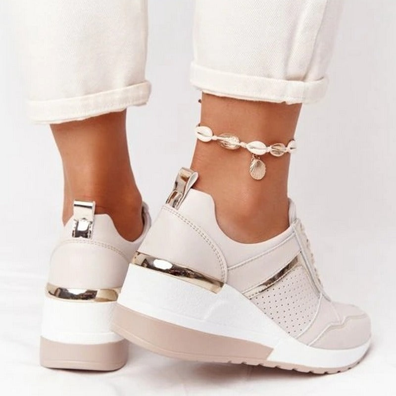White sneakers with gold accents worn by a person on a white background