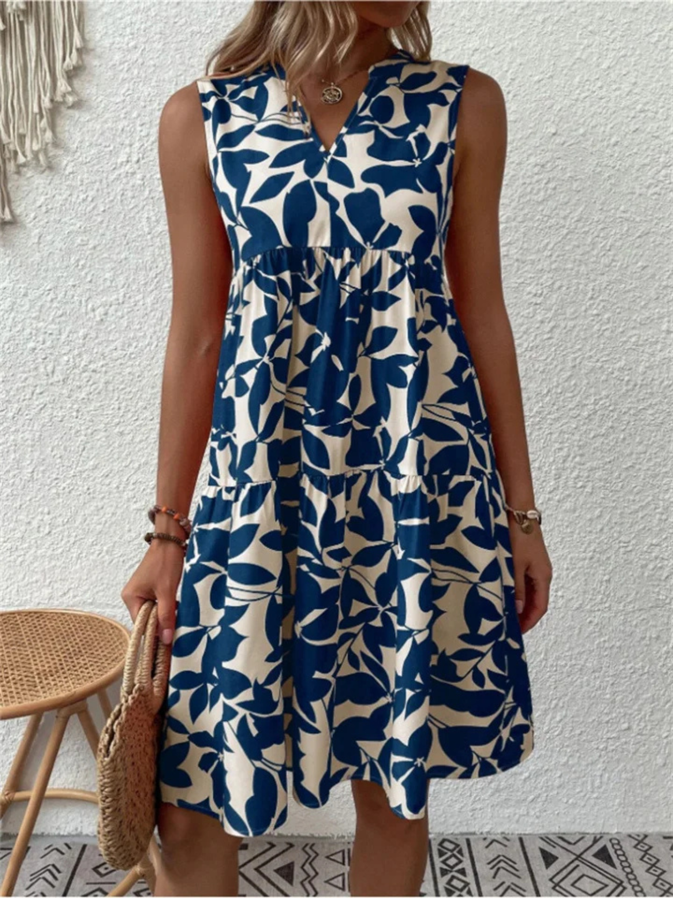Woman wearing a blue and white leaf-patterned dress against a white wall.
