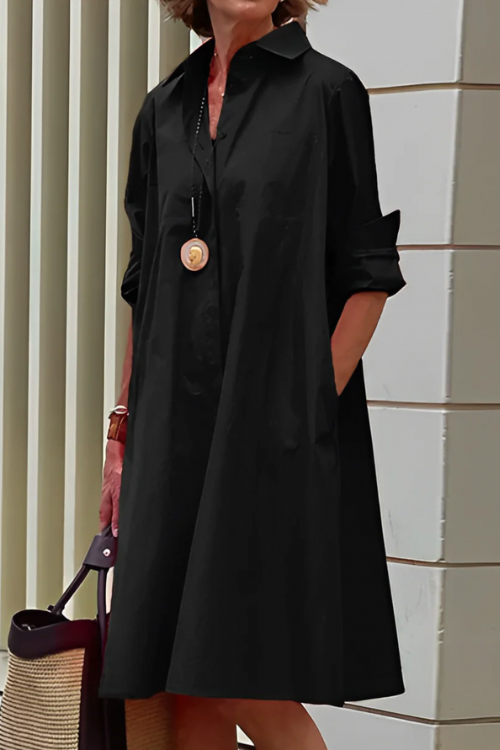 Person wearing a black dress with rolled-up sleeves, standing against a tiled wall.