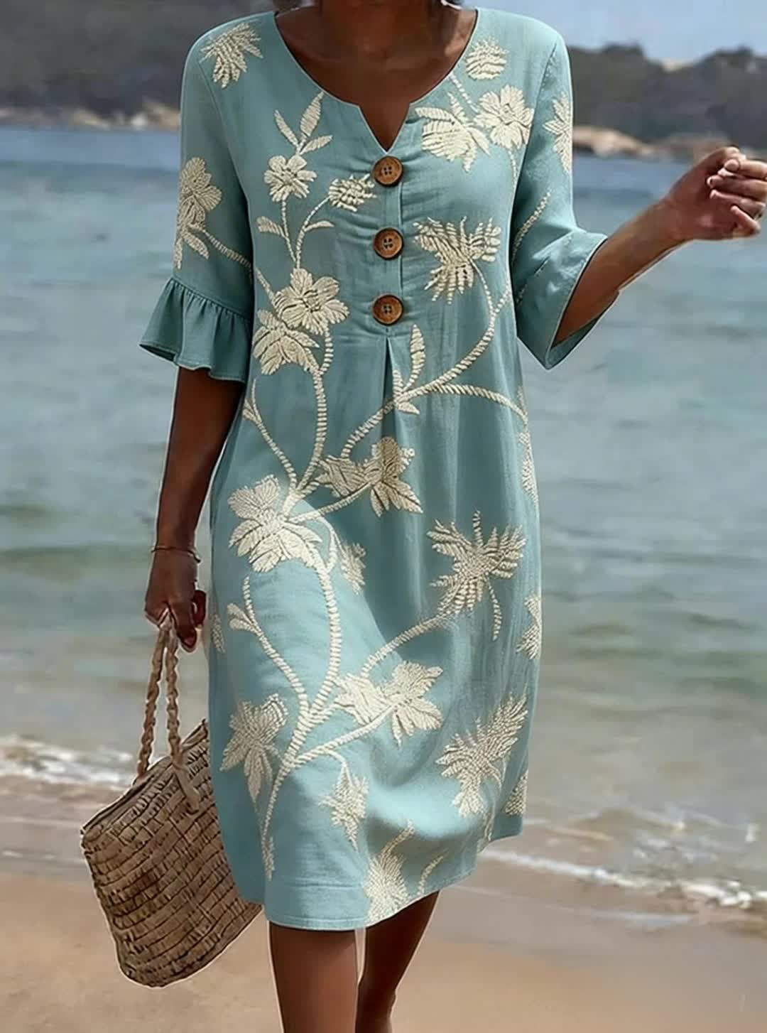 Woman wearing a light blue dress with floral patterns on a beach.