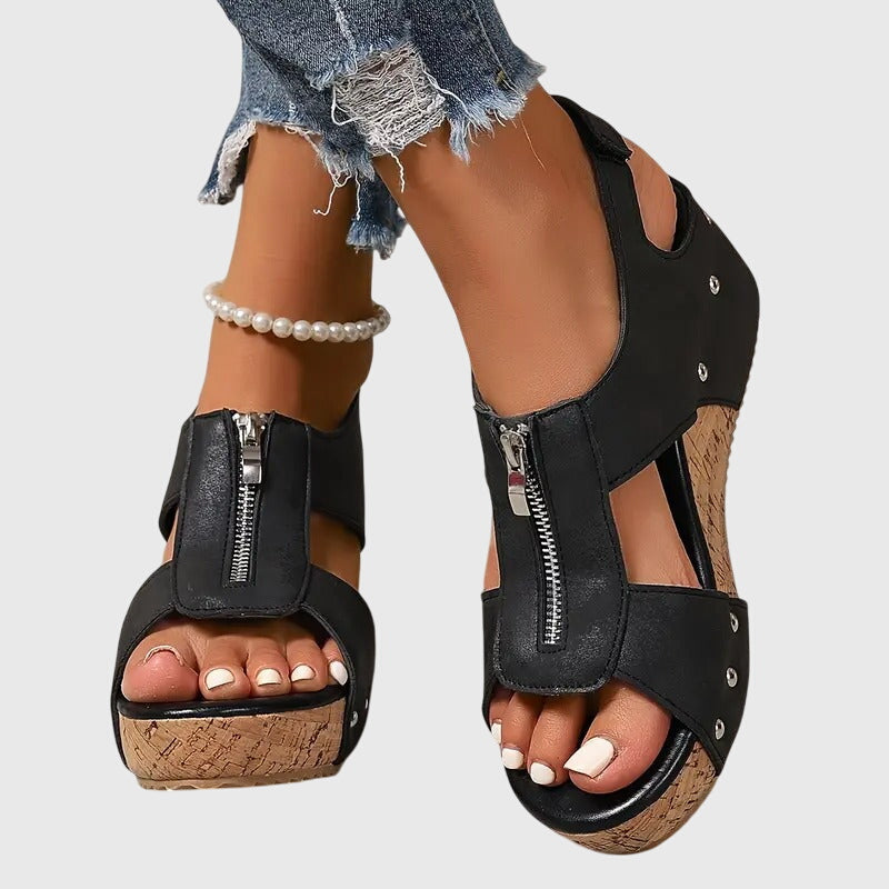 Black wedge sandals with cork soles worn by a person on a light gray background