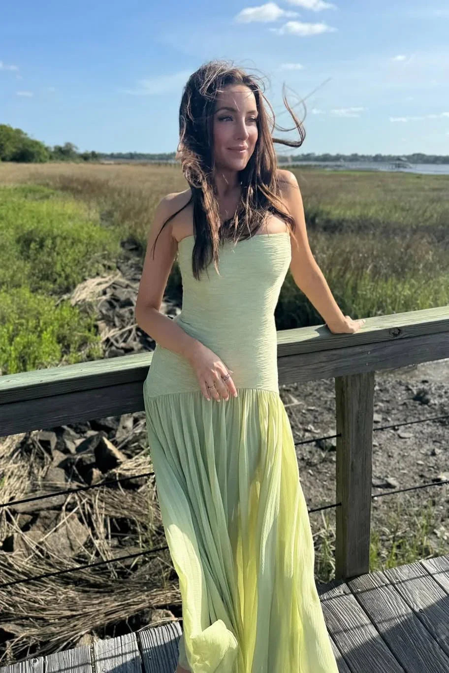 Woman in a light green dress standing on a wooden platform with a natural landscape in the background