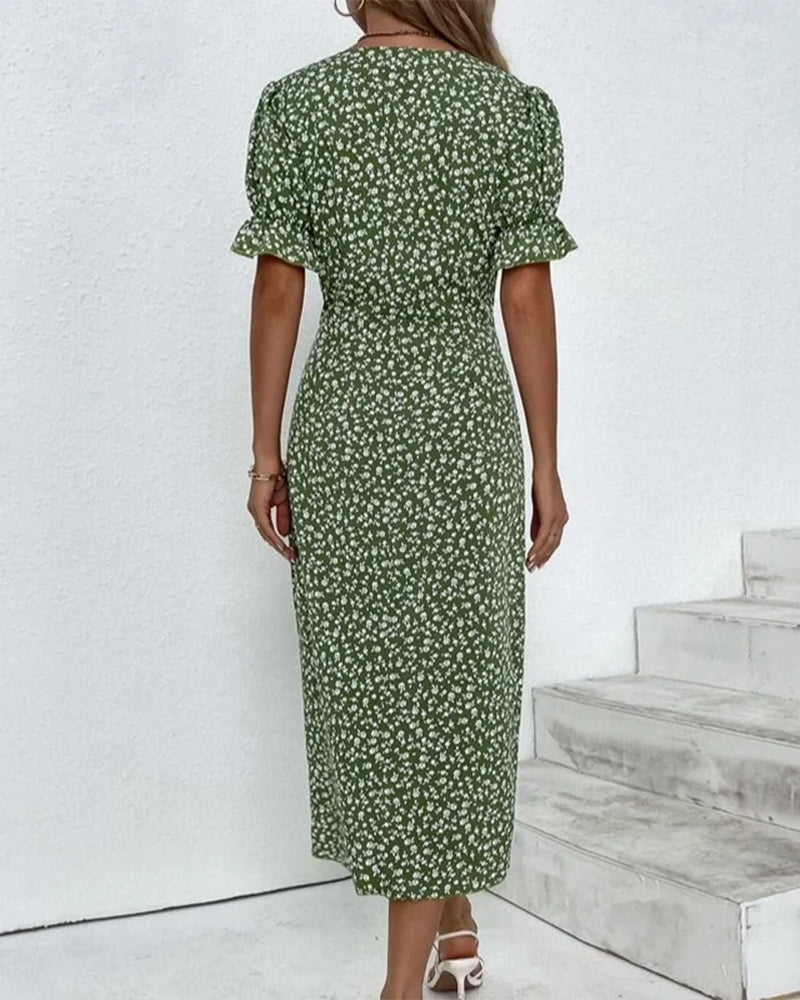 Woman wearing a green floral dress standing against a white wall with wooden steps.