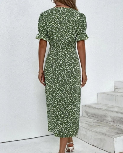 Woman wearing a green floral dress standing against a white wall with wooden steps.