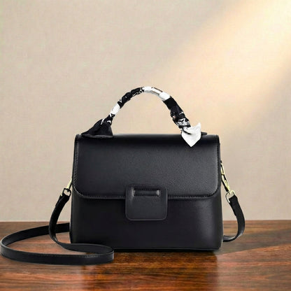Black leather top handle bag, displayed on a wooden surface against a neutral background.