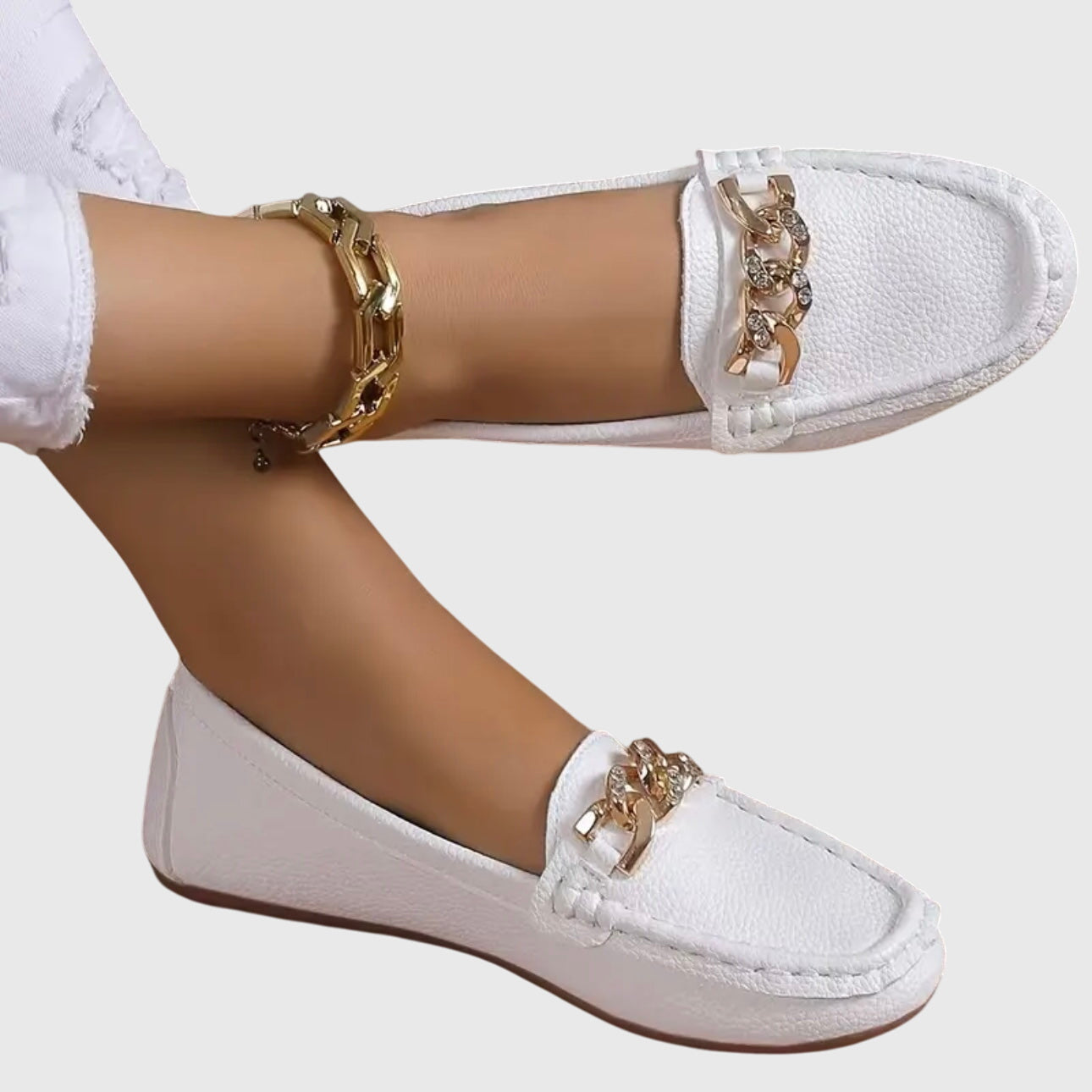 White loafers with gold embellishments worn by a person on a white background