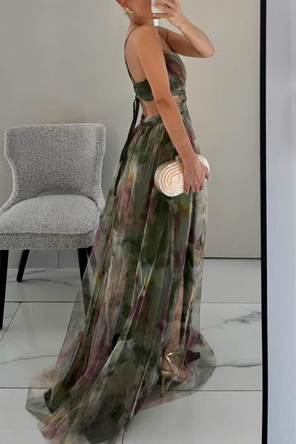 Woman in a long, sheer, multicolored dress holding a clutch in a room with a chair and white floor.
