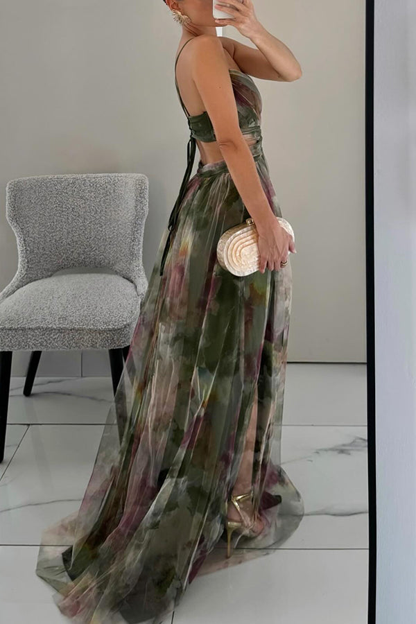 Woman in a long, sheer, multicolored dress holding a clutch in a room with a chair and white floor.