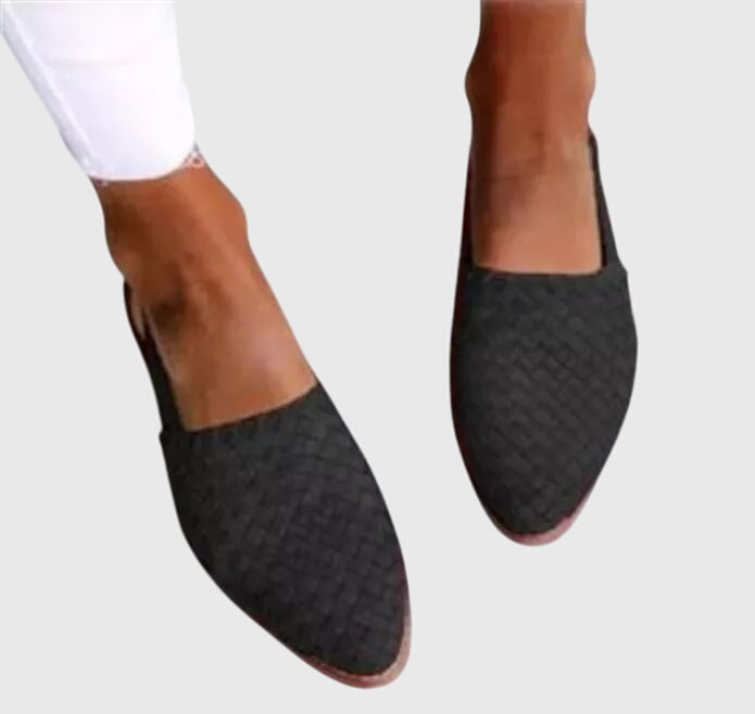 Black textured loafers worn with white pants on a light gray background