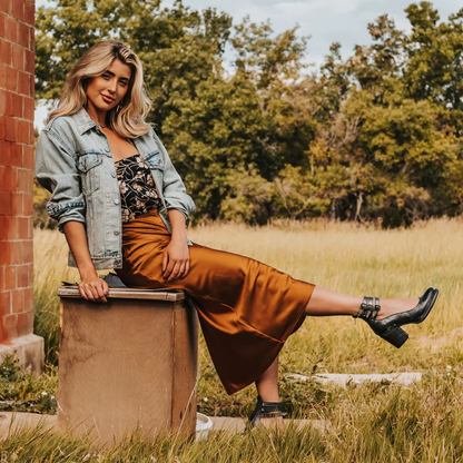 Woman in a brown dress and denim jacket sitting on a box in a natural setting