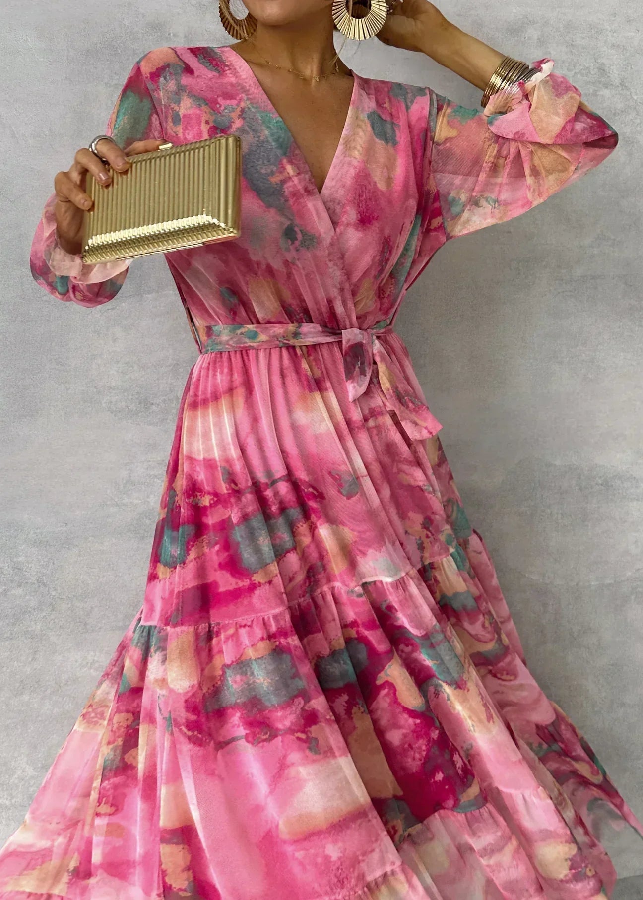 Woman wearing a pink floral dress holding a gold clutch against a gray background