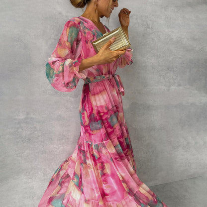 Woman wearing a pink floral dress holding a gold clutch against a gray background