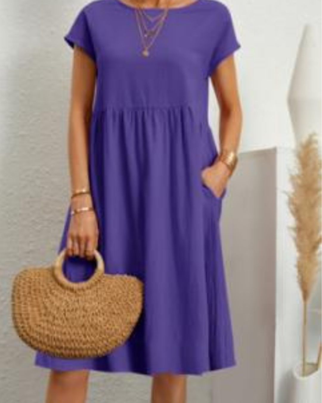 Woman wearing a purple dress holding a woven handbag against a neutral background