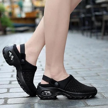 Black slip-on shoes worn by a person on a paved outdoor surface
