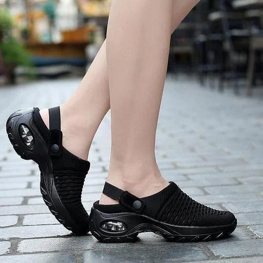 Black slip-on shoes worn by a person on a paved outdoor surface