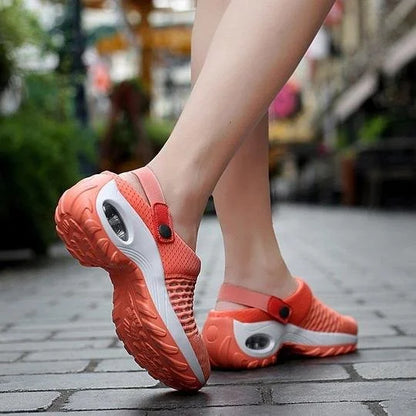 Orange clogs with white soles worn on a blurred outdoor background