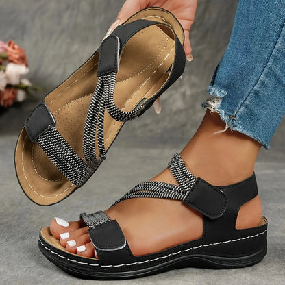 Black sandals with woven straps worn by a person on a gray surface.