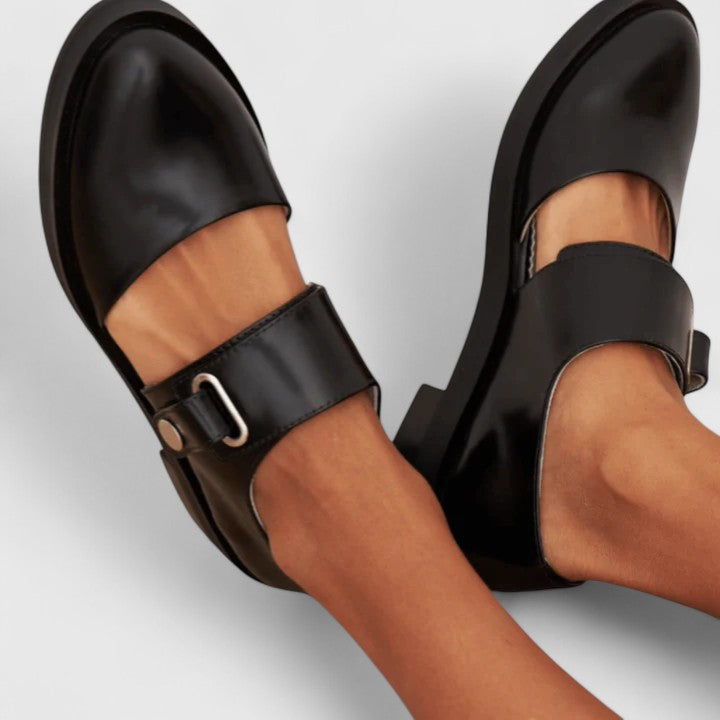 Black sandals with buckles worn by a person on a light gray background
