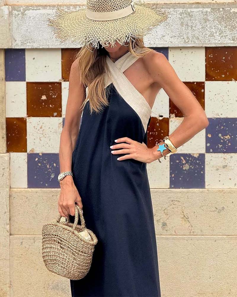 Woman in a navy dress and wide-brimmed hat holding a straw bag against a colorful tiled wall.