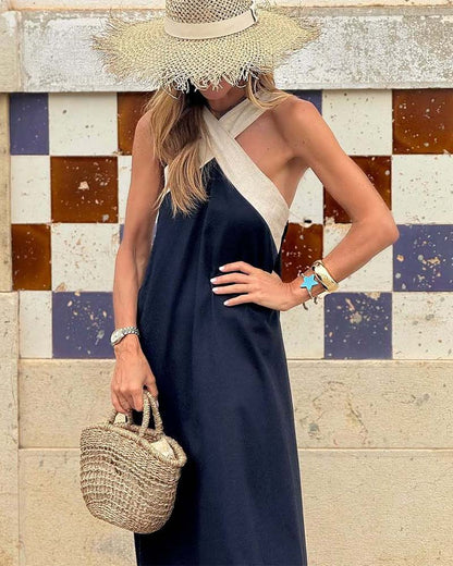 Woman in a navy dress and wide-brimmed hat holding a straw bag against a colorful tiled wall.