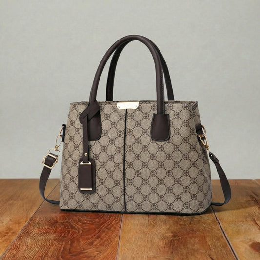 Monogram pattern shoulder bag with dark brown leather handles and detachable crossbody strap, structured women’s handbag on wooden surface.