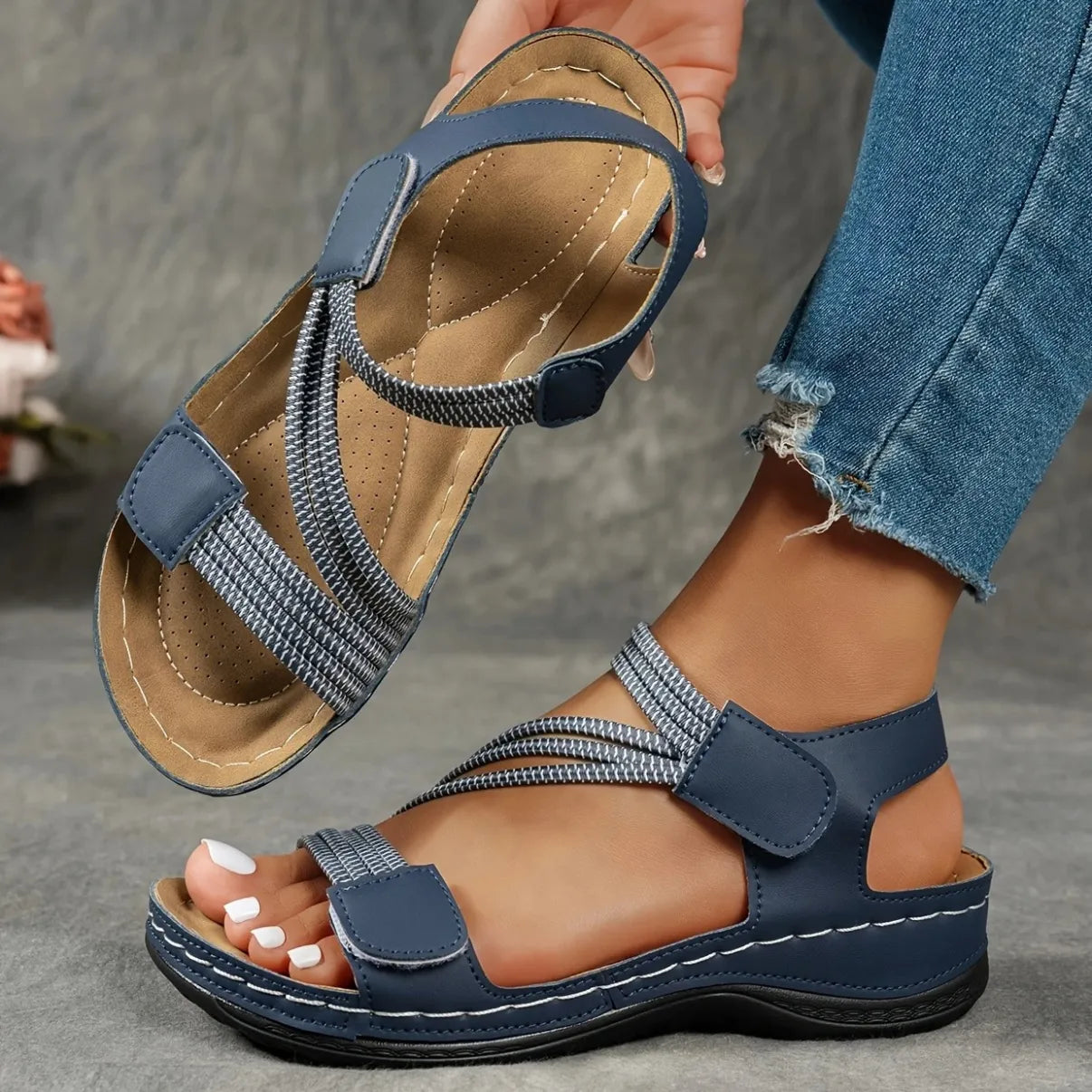 Blue sandals worn with ripped jeans on a gray background