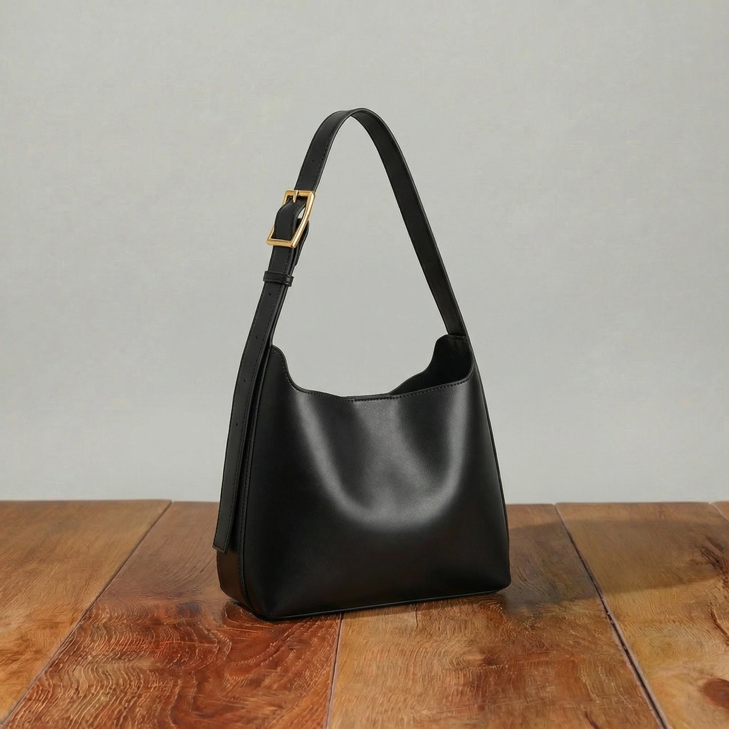 Black leather hobo bag with soft curved silhouette and adjustable shoulder strap, minimalist women’s shoulder purse displayed on wooden table.
