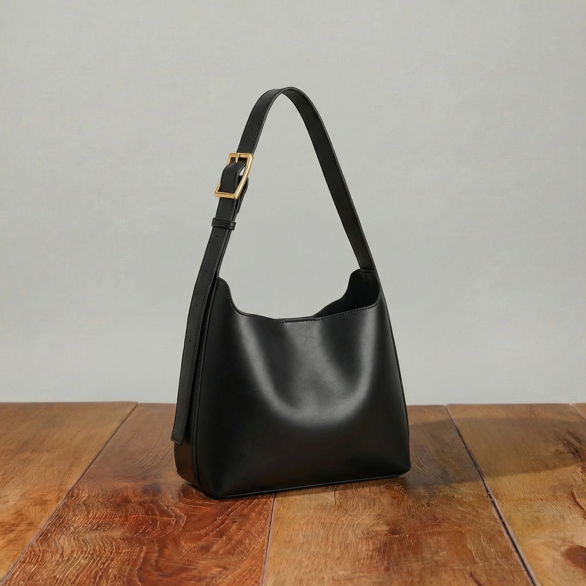Black leather hobo bag with soft curved silhouette and adjustable shoulder strap, minimalist women’s shoulder purse displayed on wooden table.
