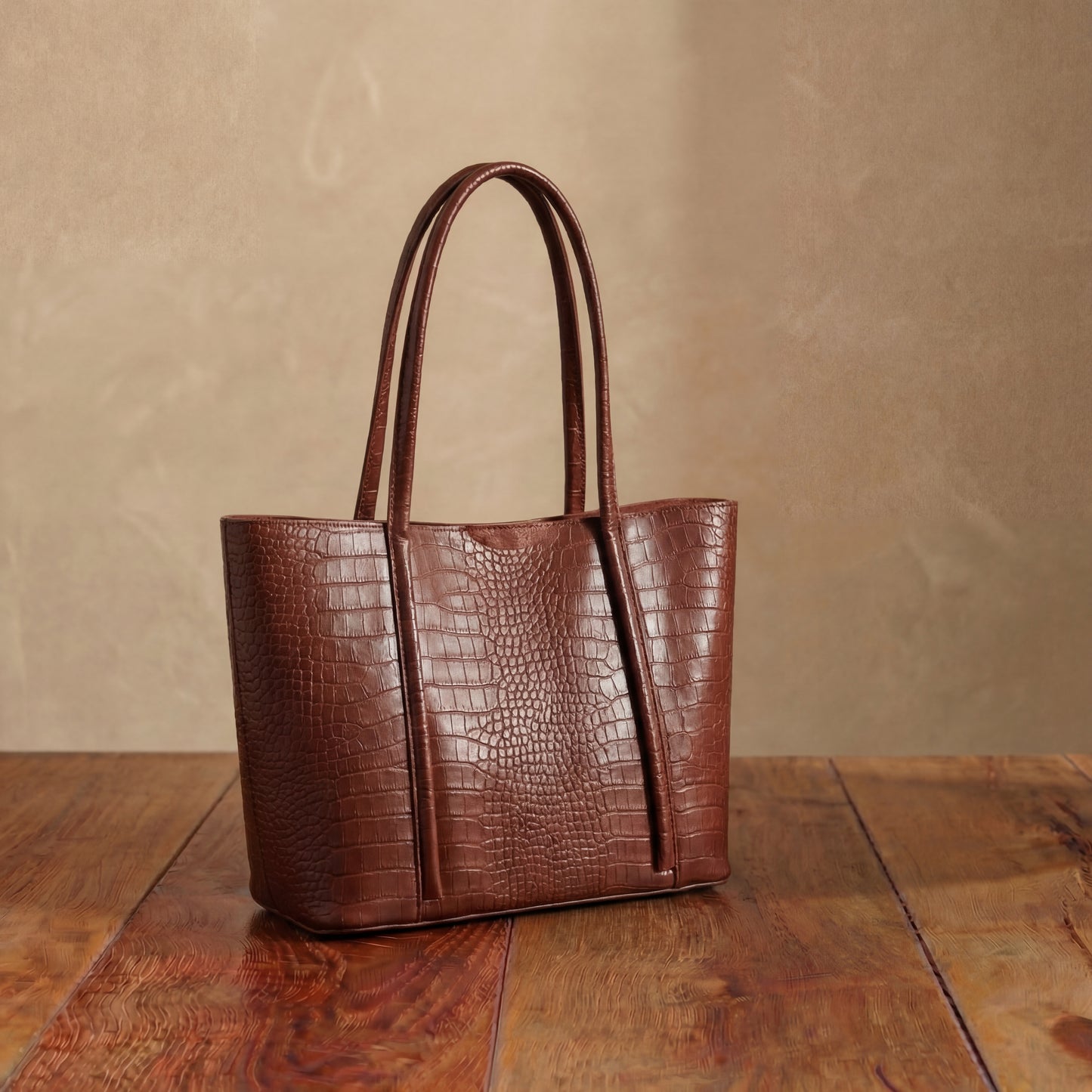 Brown embossed leather tote bag with long shoulder handles, structured textured women’s handbag in rich vintage tone displayed on wooden table.
