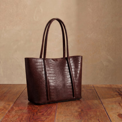 Dark brown leather tote bag on a wooden surface with a beige background