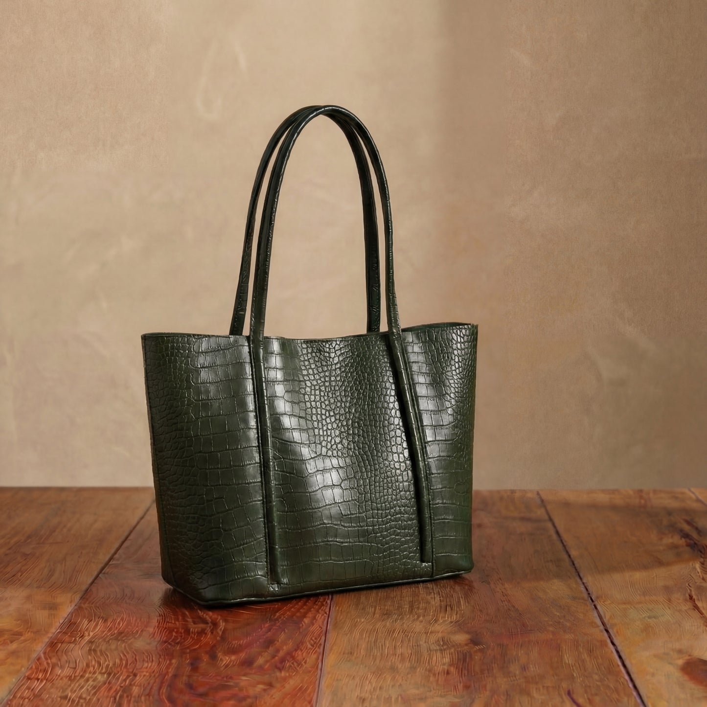 Green embossed leather tote bag with long shoulder straps, structured textured handbag displayed on wooden table.
