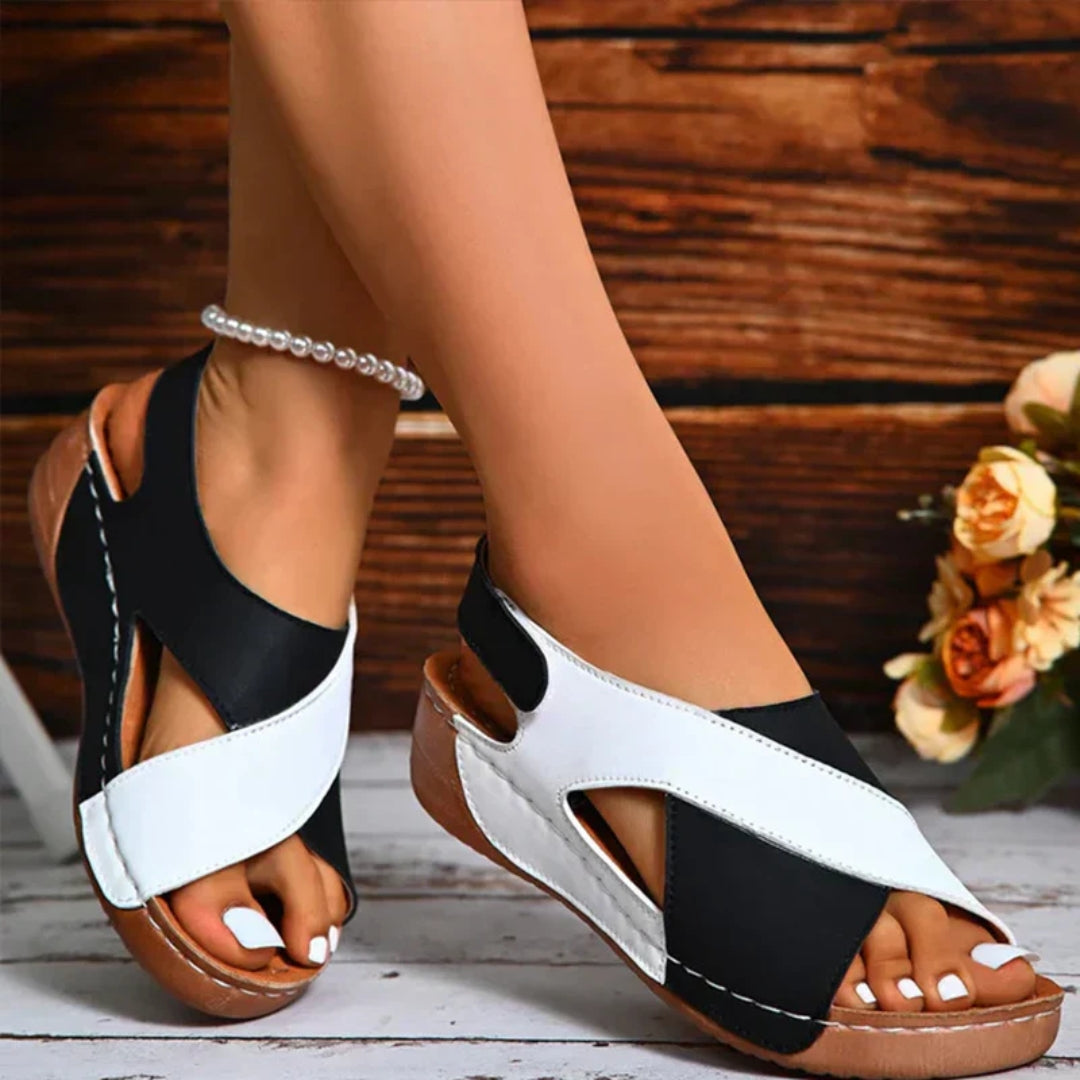 Black and white sandals worn by a person on a wooden floor with a blurred floral background