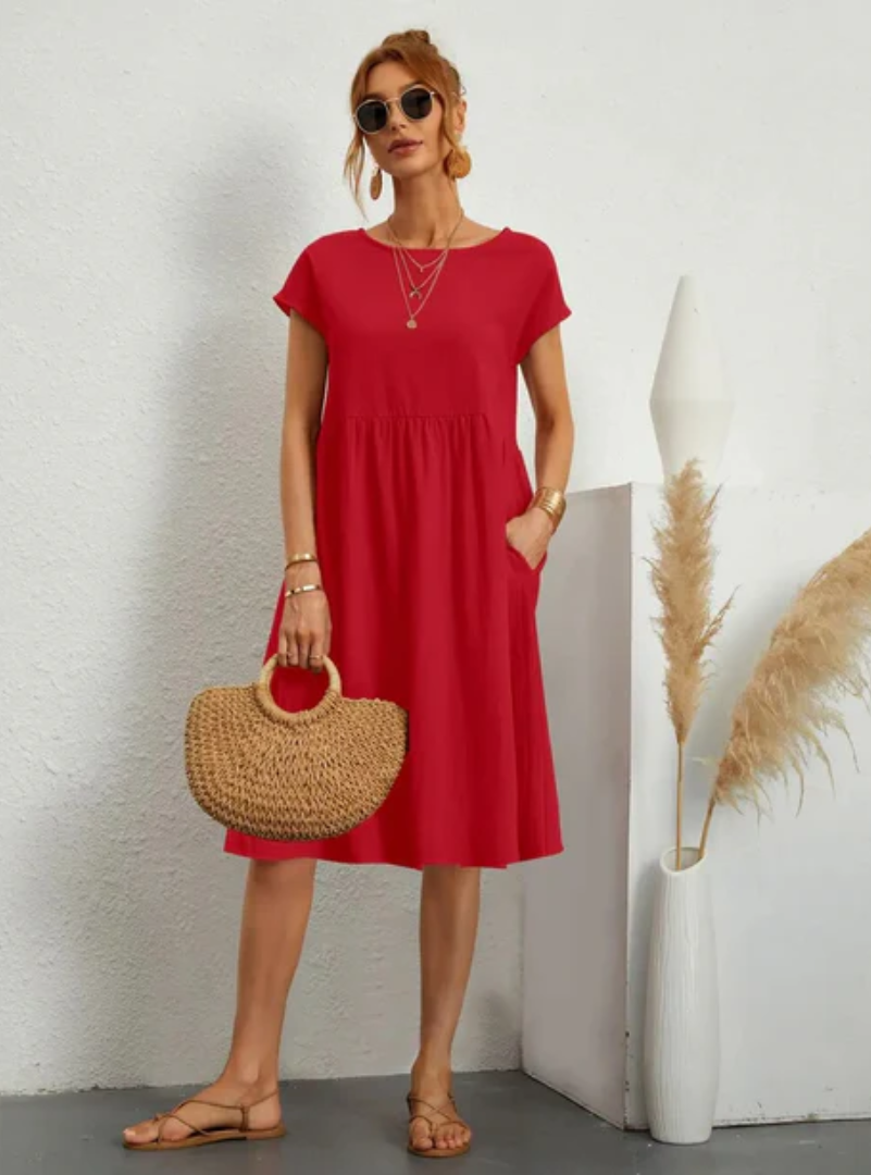 Woman in a red dress holding a straw bag against a white wall with decorative elements.