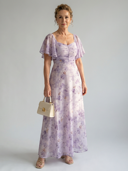 Woman wearing a light purple floral dress holding a beige handbag against a plain background
