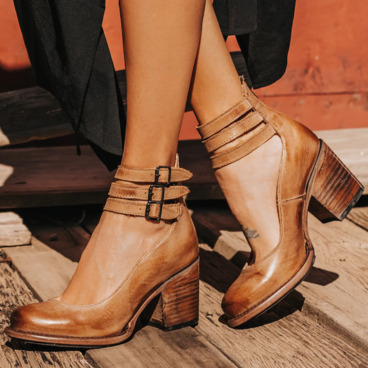Brown leather ankle boots with strap details on a wooden floor.