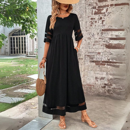 Woman wearing a black dress with sheer sleeves against a brick wall.