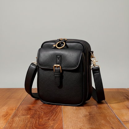 Black leather crossbody bag on a wooden surface with a gray background