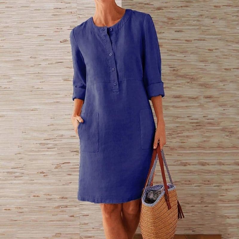 Woman wearing a blue dress holding a woven bag against a wooden panel background