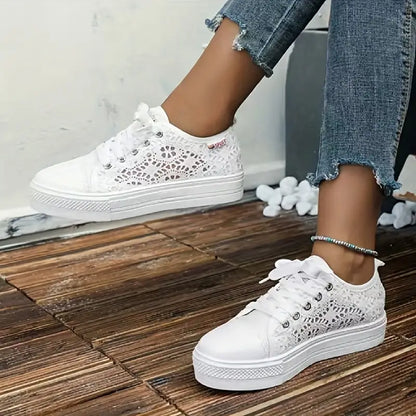 White lace-up sneakers worn with blue jeans on a wooden floor.