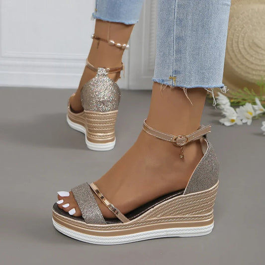 Glittery wedge sandals worn with denim jeans on a neutral background