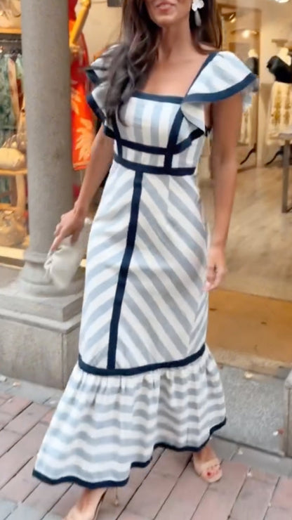 Woman wearing a white and blue striped dress with ruffled shoulders in an urban setting.