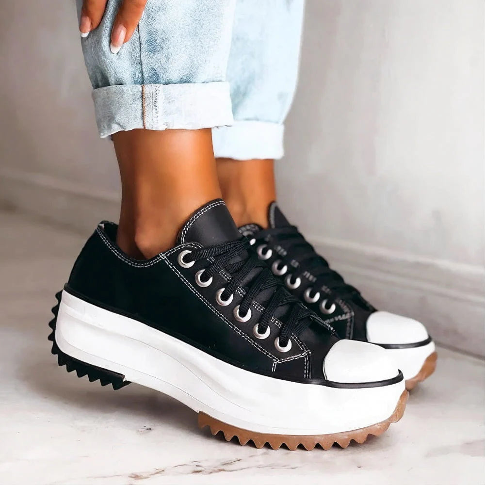 Black sneakers with white soles worn by a person on a light background