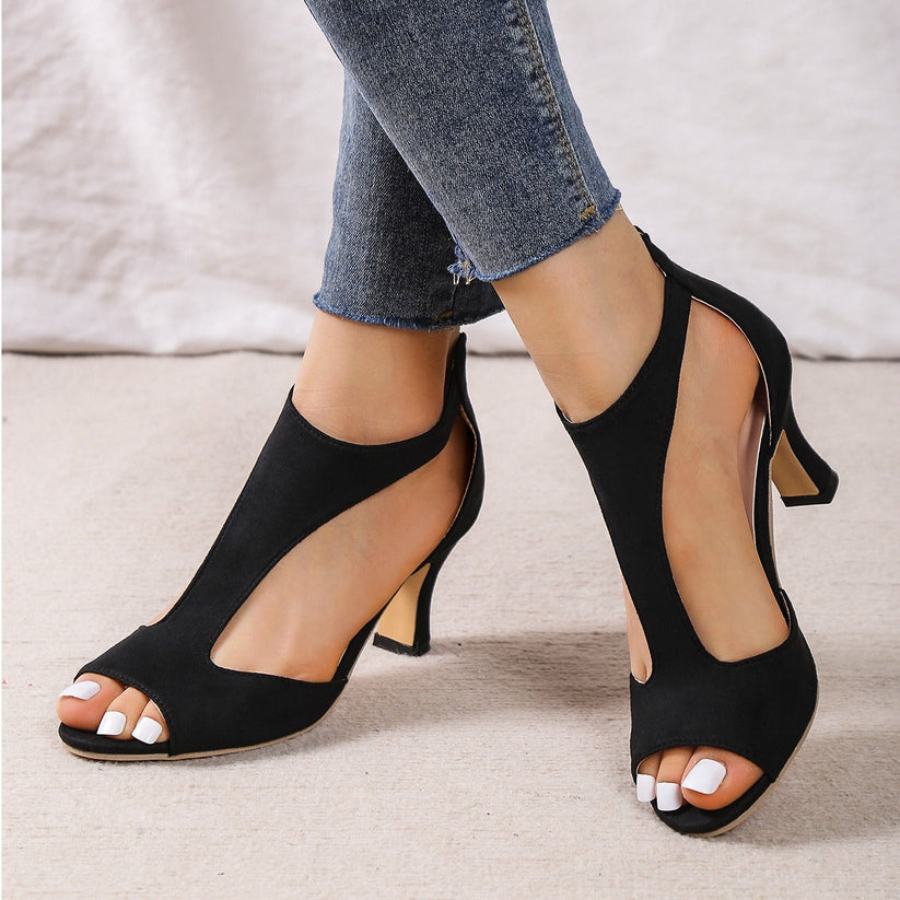 Black open-toe high-heeled shoes worn with blue jeans on a neutral background