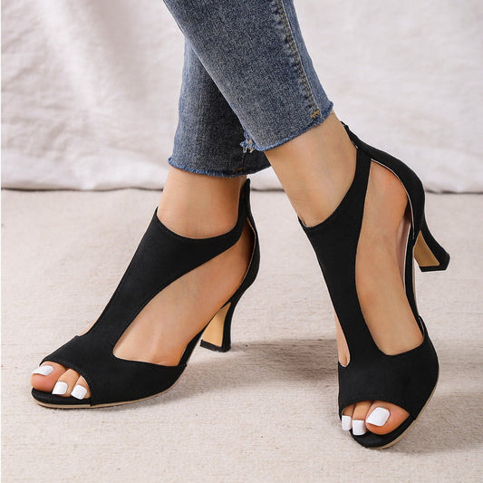 Black open-toe high-heeled shoes worn with blue jeans on a neutral background