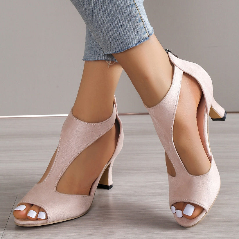 Beige high-heeled shoes worn with denim jeans on a neutral background