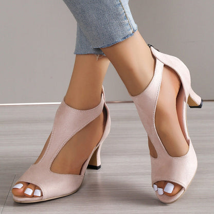 Beige high-heeled shoes worn with denim jeans on a neutral background