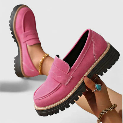 Pink loafers with black soles held by a hand against a light background