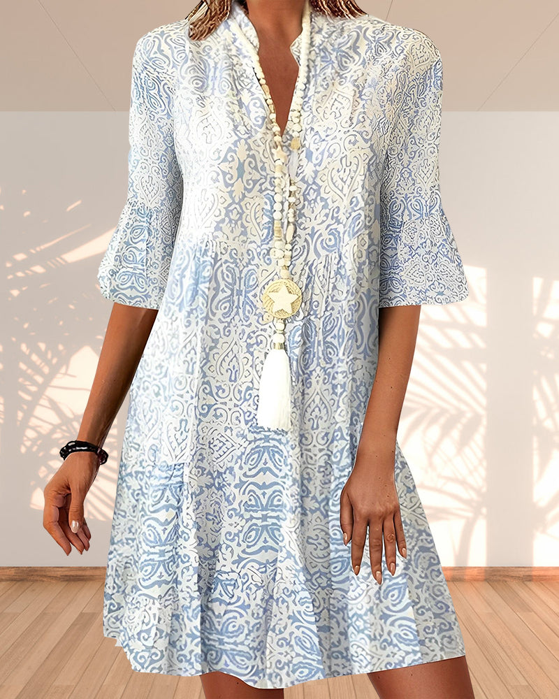Woman wearing a white dress with blue patterns in a bright room.